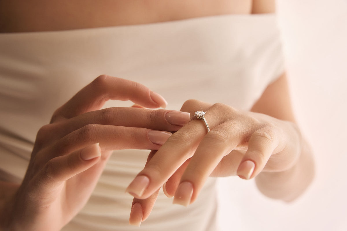 A woman slipping a solitaire engagement ring onto her ring finger against a soft light background